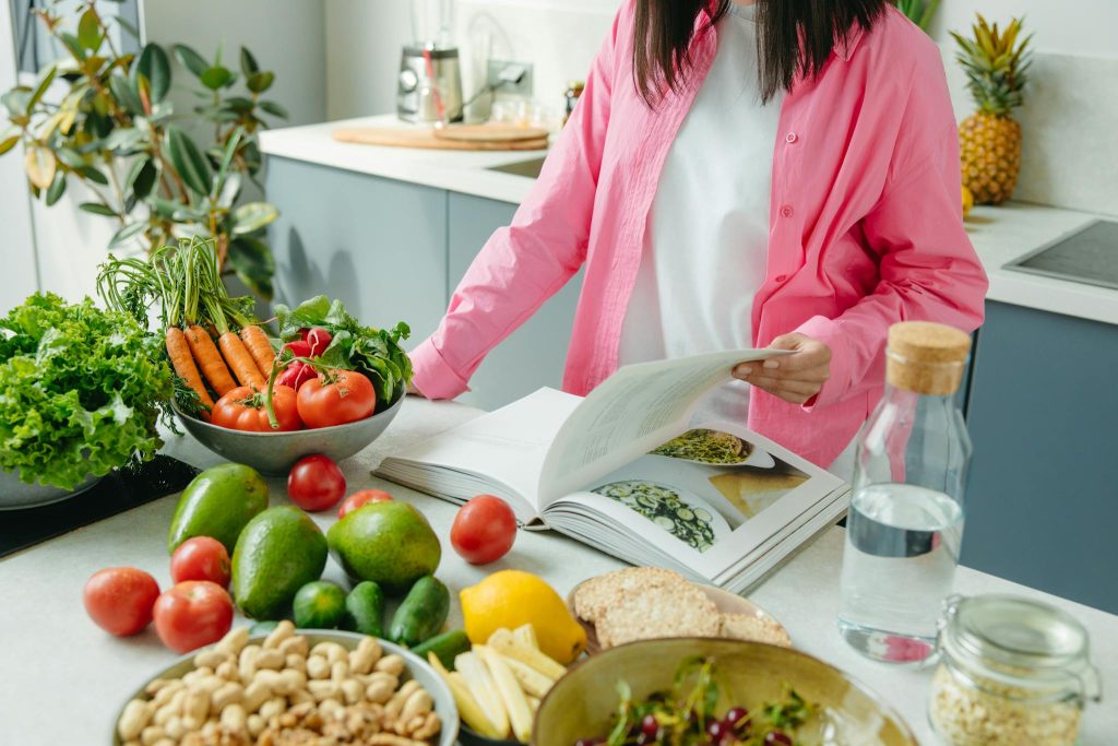 Woman reading healthy recipe book with fresh vegetables and fruits for weight loss meal planning