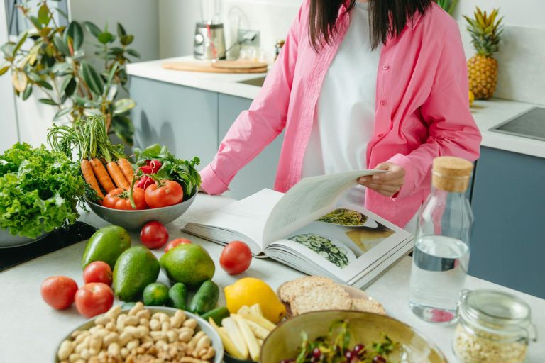 Woman reading healthy recipe book with fresh vegetables and fruits for weight loss meal planning